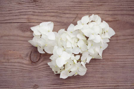 White flower in heart shape on wooden background. Valentine's Day theme
