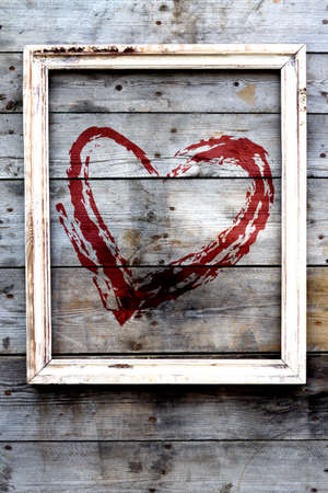 Wooden frame with red heart  on a grunge background. Drawing love symbol on wooden wall.