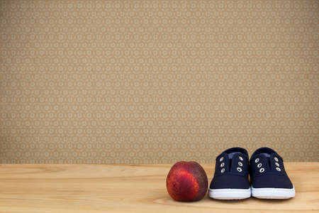 Sneakers and peach on wooden table over vintage wallpaper. Space for textの写真素材