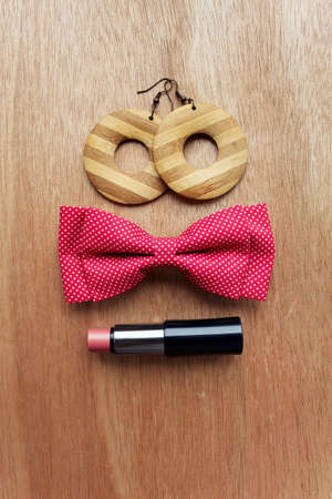 Fashion accessories on wooden surface. Earrings, bow tie, lipstickの写真素材