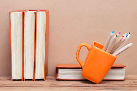 A stack of books and a mug with colored pencils on wooden table. School themeの写真素材
