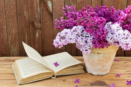 Bouquet of lilac flowers in a pot and old book on a background of vintage wooden boardの写真素材