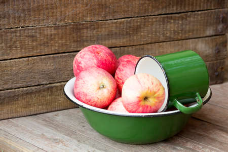 Fresh apples in a green tin bowl on wooden backgroundの写真素材
