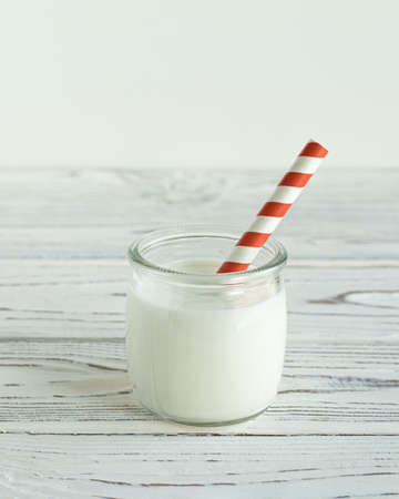Glass of milk with red and white straw on white wooden tableの写真素材