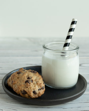 Cookies with chocolate, glass of milk with black and white straw on light wooden tableの写真素材