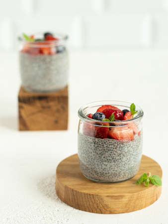 Vegan chia pudding with coconut milk, decorating strawberry, blueberry and mint leaves. Summer dessert on the white background. Portioned dessert in the glass jars. wooden propsの写真素材