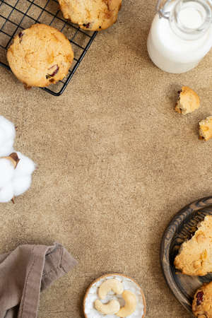 Oatmeal cookies with cranberry, cashew and white chocolate. Bottle of milk, cooling rack with cookies, kitchen towel, nuts and cotton flower. Space for text. food frameの写真素材