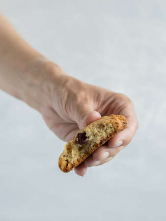Female hand holding a bitten cookie with cranberry, cashew nuts and white chocolateの写真素材