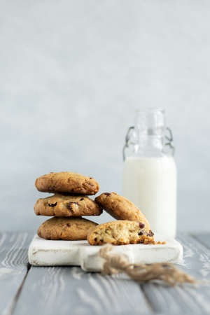 Stack of oatmeal cookies with cranberry, cashew nuts and white chocolate on a white wooden cutting board. Glass bottle of milk on the background. gray wooden tableの写真素材