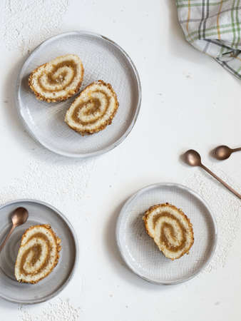 Pieces of biscuit roll with apple jam on a plates. Checkered kitchen, fresh green apple, cinnamon and teaspoons on white background, flat layの写真素材