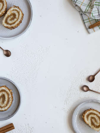 Pieces of biscuit roll with apple jam on a plates. Checkered kitchen towel, cooper colored teaspoons and stick of cinnamon on a white background. Flat lay, space for textの写真素材