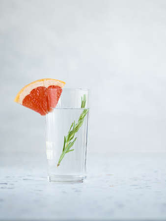 High glass of water decorated oiece of grapefruit and branch of rosemary inside. Terrazzo table, gray background. copy spaceの写真素材