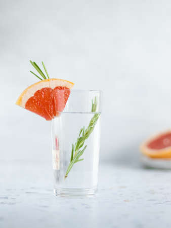 High glass of water decorated oiece of grapefruit and branch of rosemary inside. Terrazzo table, gray background. copy spaceの写真素材