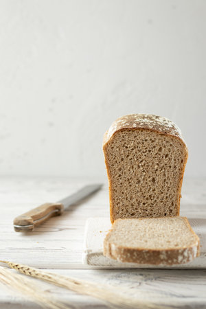 Cut loaf of rye and wheat sourdough bread on a white cutting board. Bread knife and ears of wheat on a wooden table. Space for textの写真素材
