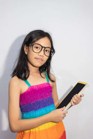 Child  girl  with glasses, colorful dresses holding a book on the white.の写真素材