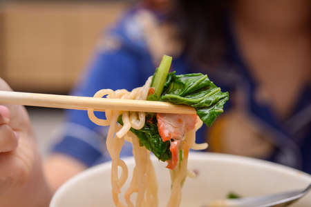 Chopsticks tossed pork noodles with vegetables and blurry background.