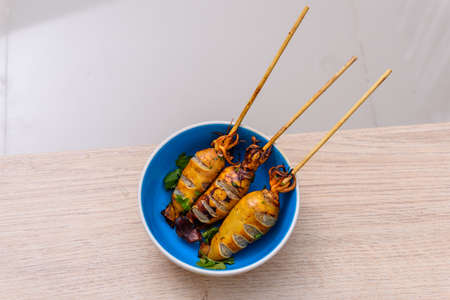 Grilled squid on skewers in blue bowl on wooden tableの写真素材