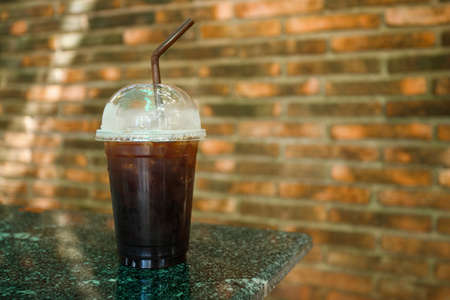 Black coffee in clear plastic mug on red brick background terrazzo table.