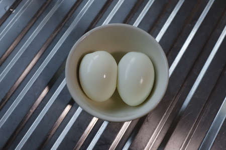 Two peeled hard-boiled eggs in a bowlの写真素材