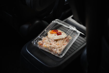 A clear lunch box with a fried egg, placed inside a car.