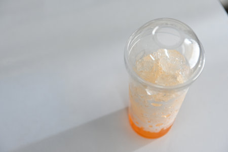 Orange juice with ice in a clear plastic cup, left over from drinking.の写真素材