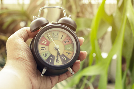 retro clock and alarm vintage color tone in hand on garden background,with copy space