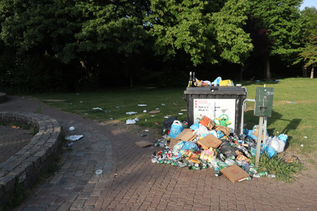 Rubbish next to rubbish bin in park with recreationists on lawnのeditorial素材