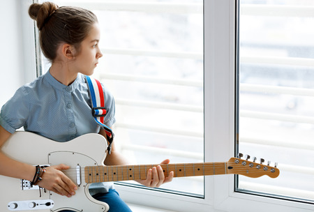 Beautiful young girl with a guitar near the window.