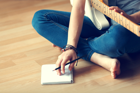 Young girl composes music while sitting on the wooden floor.の写真素材