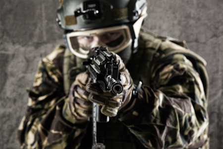 A special forces soldier holds a gun in his hands and looks into the camera.