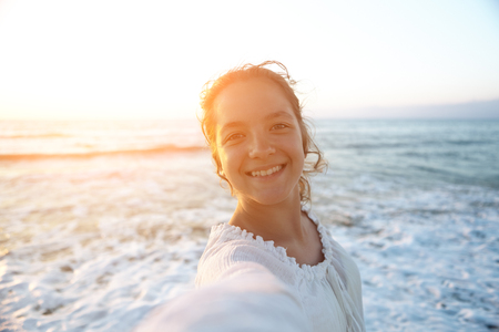 A young beautiful girl does selfie on the background of the sea.  He looks at the camera and smiles.の写真素材