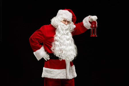 Christmas concept. Santa Claus holds a lantern in his hand and looks into the camera on a black background.の写真素材