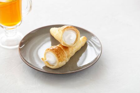 Puff pastry horn with white cream. Fresh dessert roll with cream or meringue and tea with lemon on a...