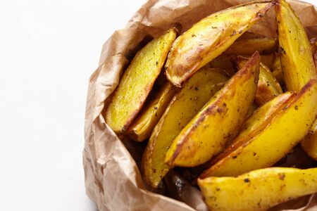 Sliced homemade french fries in a brown paper bag on a white background. Fried potatoes.