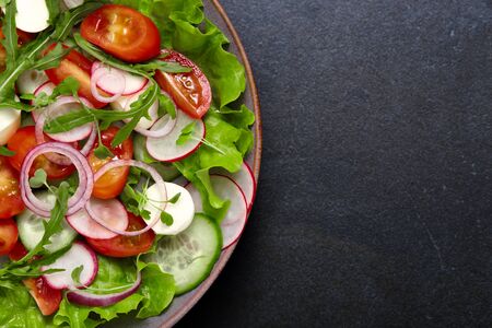 Healthy fresh salad with radish, cucumber, cherry tomato and mozzarella on a dark color background. Homemade food. The concept of a delicious and healthy diet.の写真素材