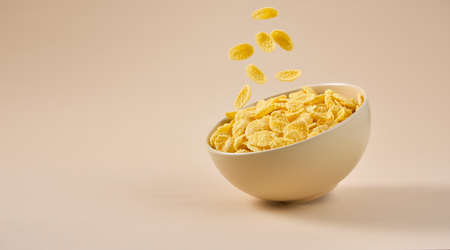 Traditional breakfast with cornflakes. Cornflakes falling into a bowl on a light beige background.の写真素材