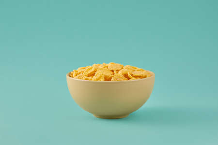 Traditional breakfast with cornflakes. Cornflakes in a light beige bowl on a colored turquoise...