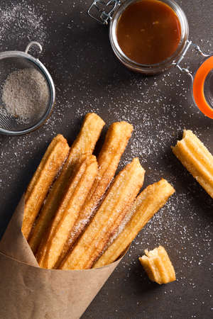 Churros with sugar, cinnamon and caramel on a dark background. Top viewの写真素材