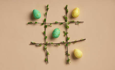 Easter eggs in a frame made of spring branches on a beige background. Tic-tac-toe game. Easter theme...