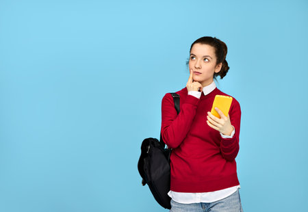 A girl student with a cell phone in her hand looks away pensively. Isolated on a blue background.