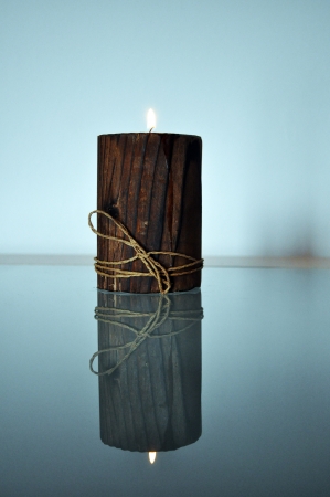 Candle in a wooden candlestick is reflected in a glass tableの写真素材