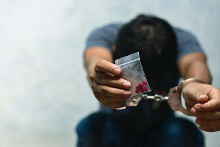 Drug dealer under arrest confined with handcuffs and hands, sale of drugs is punishable by law.