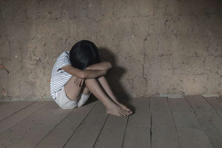 Little girl crying sitting on the floor with a grunge old wall backgroundの写真素材
