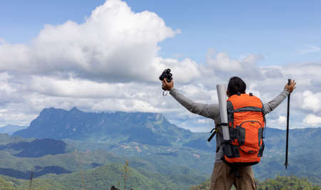 Young man with backpack and holding a binoculars looking on top of mountain layered
