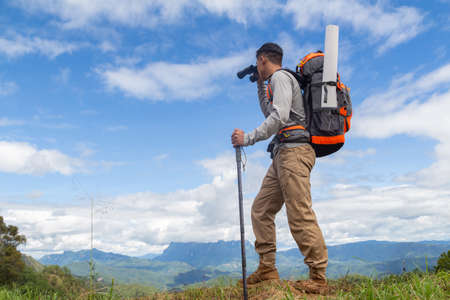 Young man with backpack and holding a binoculars looking on top of mountain layered