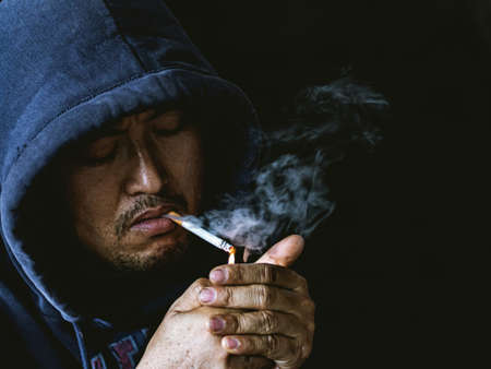 Close up portrait of young man smoking cigarette a black background