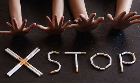 The word stop spelled using cigarettes on black background with stop hands