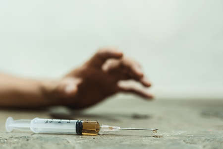 Male of a drug addict and a syringe with narcotic syringe lying on the floor. Anti drug concept.の写真素材