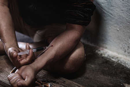 Men of a drug addict and a syringe with narcotic syringe sitting on the floor. Anti drug conceptの写真素材