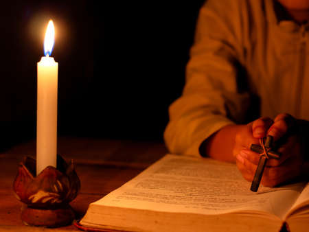 Child praying to the GOD while holding a crucifix symbol with lighting candle at night time.
